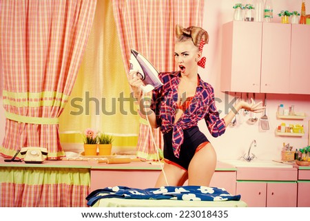 Charming pin-up girl ironing her dress on a glamorous pink kitchen. Retro style. Fashion.