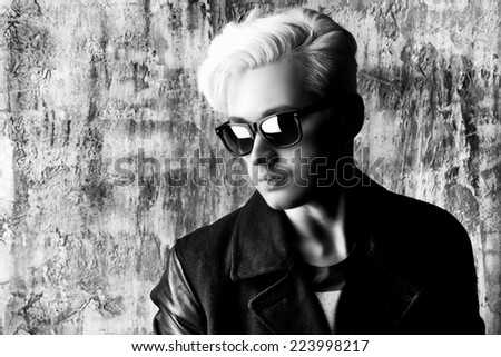 Black-and-white portrait of a fashionable male model with blond hair wearing black jacket and sunglasses. Men\'s beauty, fashion.