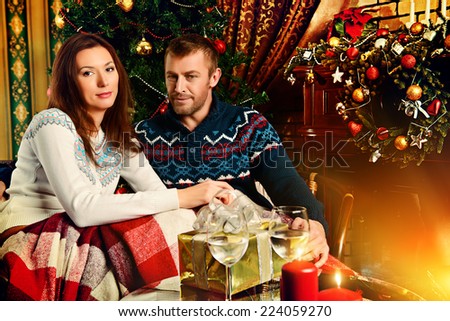 Happy married couple spend a romantic evening by the fireplace next to the Christmas tree.