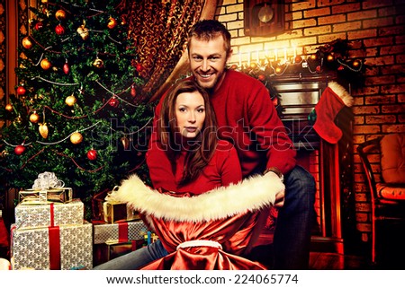 Happy married couple spend a romantic evening by the fireplace next to the Christmas tree.