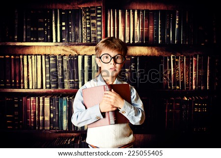 Smart boy stands in the library by the bookshelves with many old books. Educational concept. Science.