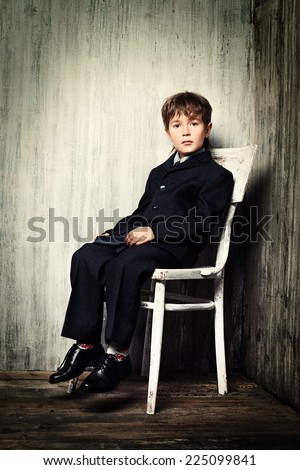 Art portrait of a boy in a suit sitting on a white chair. Educational concept.