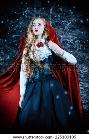 Beautiful blonde woman in  old-fashioned dress and red cloak in a fairy forest.
