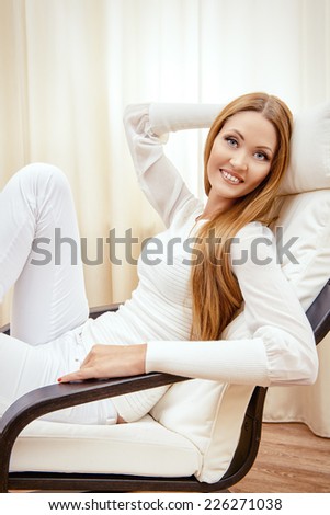 Happy young woman resting at home in a comfortable chair.