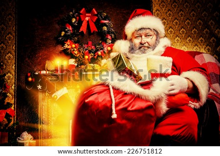 Tired Santa Claus stands by the fireplace with a bag of gifts. Christmas home decoration.