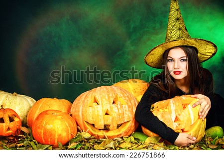 Pretty teen girl in a costume of witch standing with pumpkins over dark smoky background. Halloween.