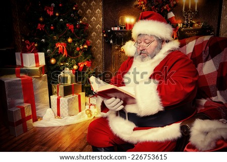 Santa Claus sitting in a room decorated for Christmas, and carefully read the boojk. Christmastime.