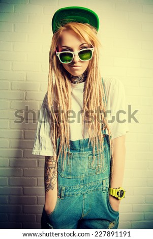Modern teenage girl with blonde dreadlocks standing by the brick wall. Jeans style. Modern generation.