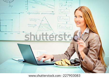 Beautiful businesswoman working in the office with a laptop and eating cookies.