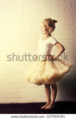 Little girl in a tutu by the white brick wall. Ballet school.