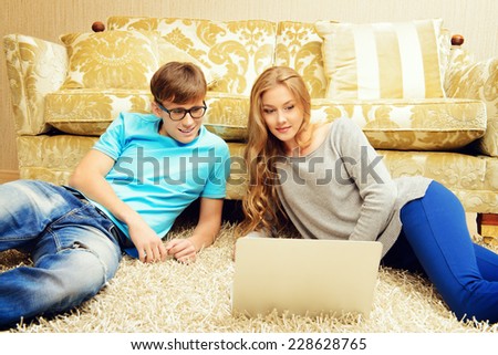 Happy young couple websurfing on internet with laptop. They sit in the cozy living room of their home.