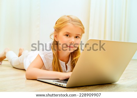 Cute five year old girl lying on a floor and playing with her laptop. Home.