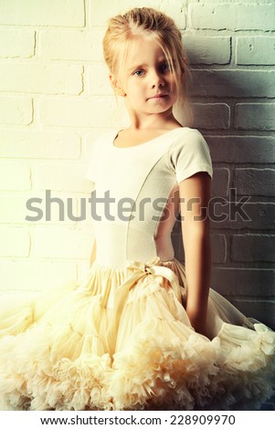 Little girl in a tutu by the white brick wall. Ballet school.