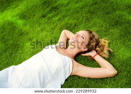 Beautiful smiling woman lying on a grass outdoor. She is absolutely happy.