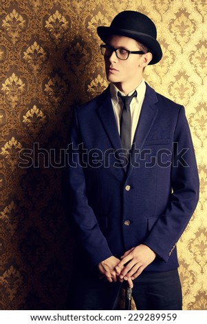 Portrait of a handsome young man in elegant suit and bowler hat posing over vintage background.