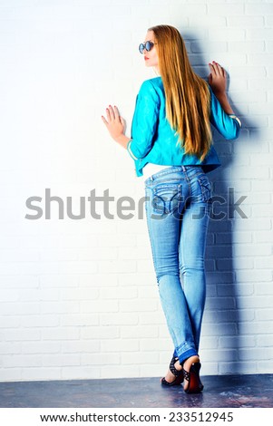 Full length portrait of a stunning young woman posing by the white brick wall. Jeans style. Beauty, fashion.