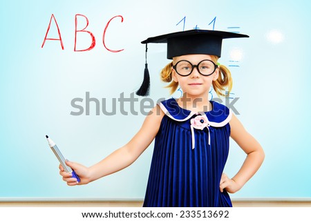 Cute little student girl in academic hat during the lesson at school. Educational concept.