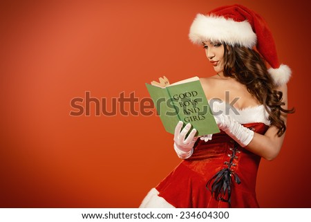 Attractive young woman in Santa Claus costume reading a list of good boys and girls. Red background. Christmas.