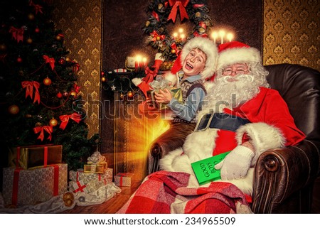 Santa Claus and laughing cute boy sitting in Christmas room with gifts. Christmas home dÃ?Â©cor.