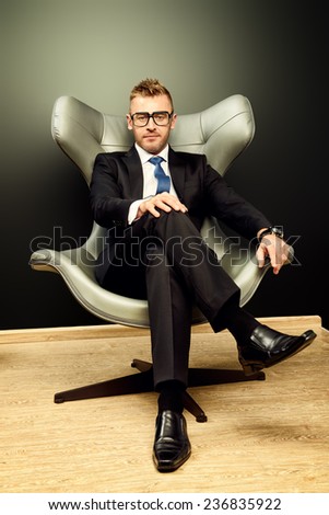 Imposing mature man in elegant suit sitting on a leather chair in a modern luxurious interior. Fashion. Business.