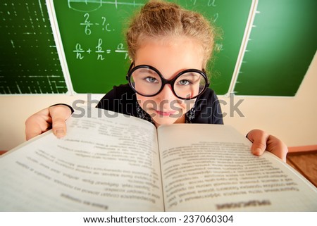 Funny schoolgirl in big round glasses opened the book and stares at the camera. Education.