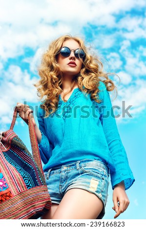 Gorgeous young woman with beautiful wavy hair wearing casual blouse and jeans shorts posing outdoor. Fashion shot.