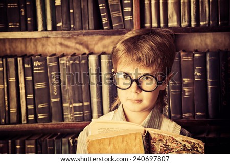 Smart boy stands in the library by the bookshelves with many old books. Educational concept. Science. Vintage style.