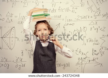 Pretty smart schoolgirl in big glasses stands with books at the blackboard. Education.