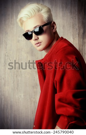 Portrait of a fashionable male model with blond hair wearing red coat and black sunglasses. Men\'s beauty, fashion.