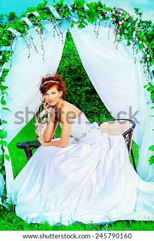 Beautiful bride with chaming red hair sitting under the wedding arch. Wedding dress and accessories. Wedding decoration.