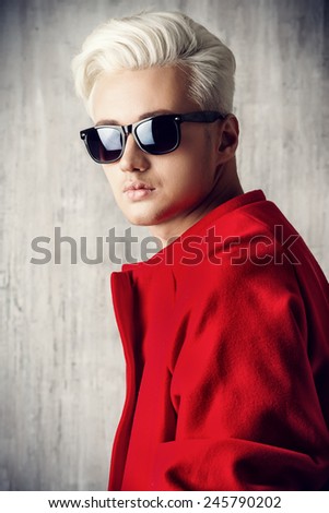 Close-up portrait of a fashionable male model with blond hair wearing red coat and black sunglasses. Men\'s beauty, fashion.