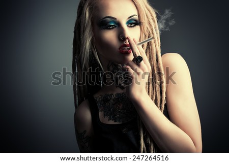 Sexy smoking girl with black make-up and long dreadlocks. Gothic style. Fashion. Cosmetics, hairstyle. Tattoo.