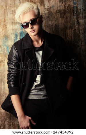 Portrait of a handsome male model with blond hair wearing black jacket and sunglasses. Urban style. Fashion.