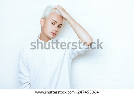 Beautiful young man with sensual look posing at studio by the white brick wall. Hairstyle, fashion.