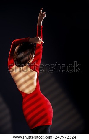 Fashion shot of a sexual woman in elegant red dress over black background.