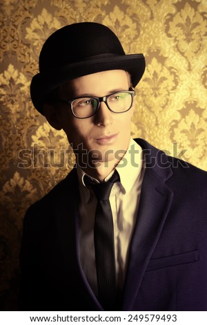 Portrait of a handsome young man in elegant suit and bowler hat posing over vintage background.