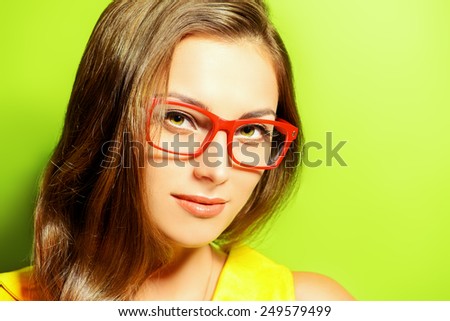 Beauty portrait of a positive young woman in spectacles and bright yellow dress over green background. Beauty, fashion. Optics.