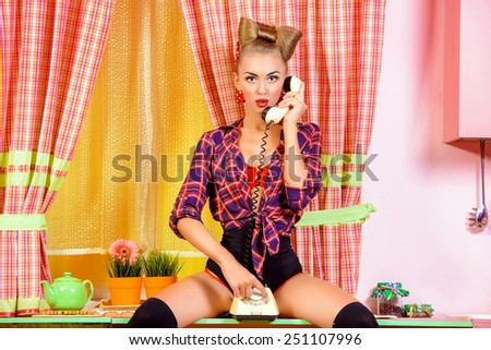 Sexy pin-up girl talking on the phone on a pink kitchen. Retro style. Fashion.