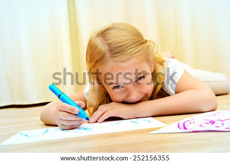 Cute girl lying on a floor and drawing on paper with colorful pens.