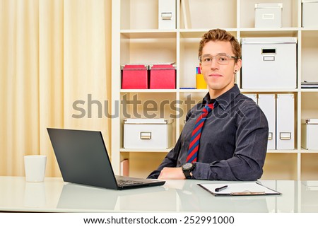 Handsome businessman working at the office on his laptop and friendly smiling at camera.