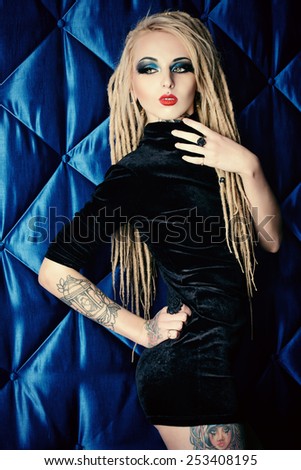 Sexual girl with black make-up and long dreadlocks wearing black dress. Gothic style. Fashion. Cosmetics, hairstyle. Tattoo.