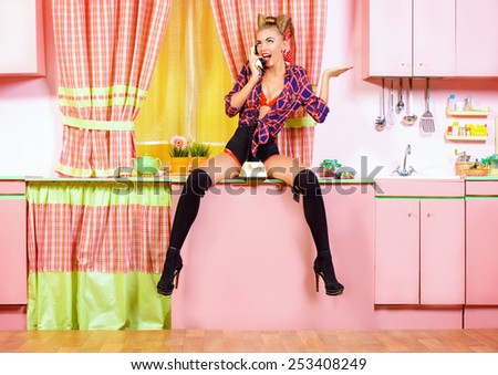 Sexy pin-up girl talking on the phone on a pink kitchen. Retro style. Fashion.