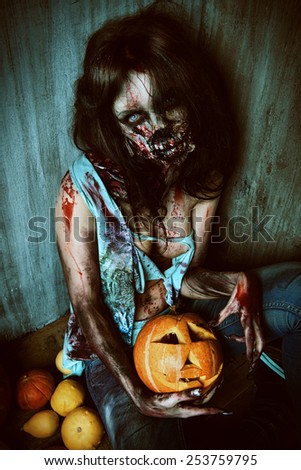 Terrible bloody zombie girl sitting by the old wall and pumpkins. Horror. Halloween.