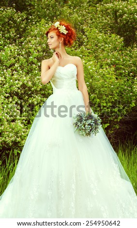 Lovely elegant red-haired bride stands on the lawn. Wedding dress and accessories.