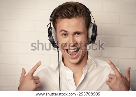 Emotional young man in white shirt listening to music in headphones with excitement.