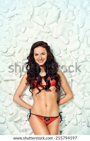 Fashion shot of a beautiful brunette woman in bikini posing over background of white paper flowers. Beauty, fashion. Spa, healthcare.