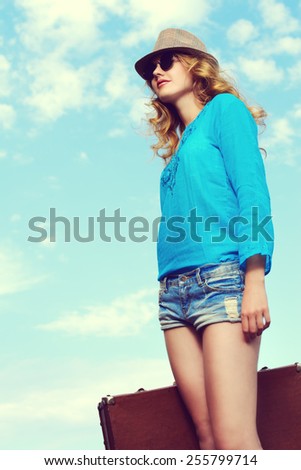 Portrait of a beautiful young woman with her old suitcase against the blue sky. Fashion shot.