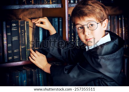 Smart boy stands in the library by the bookshelves with many old books. Educational concept. Science. Vintage style.