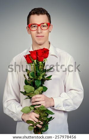 Portrait of a smiling young man in glasses holding a bouquet of red roses. Love concept.