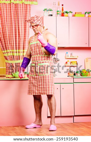 Serious muscular man in an apron standing in the pink kitchen. Love concept. Valentine's day. Women's day.
